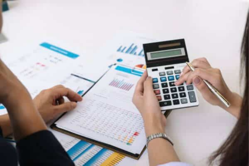 Duas pessoas analisando planejamento financeiro em uma mesa com papéis, gráficos, caderno de anotações e calculadora.