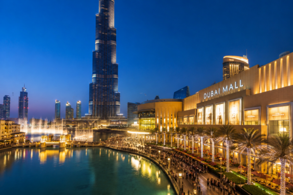 Dubai Mall iluminado ao entardecer com Burj Khalifa, Fonte de Dubai, promenade com turistas e skyline moderno de Downtown Dubai.